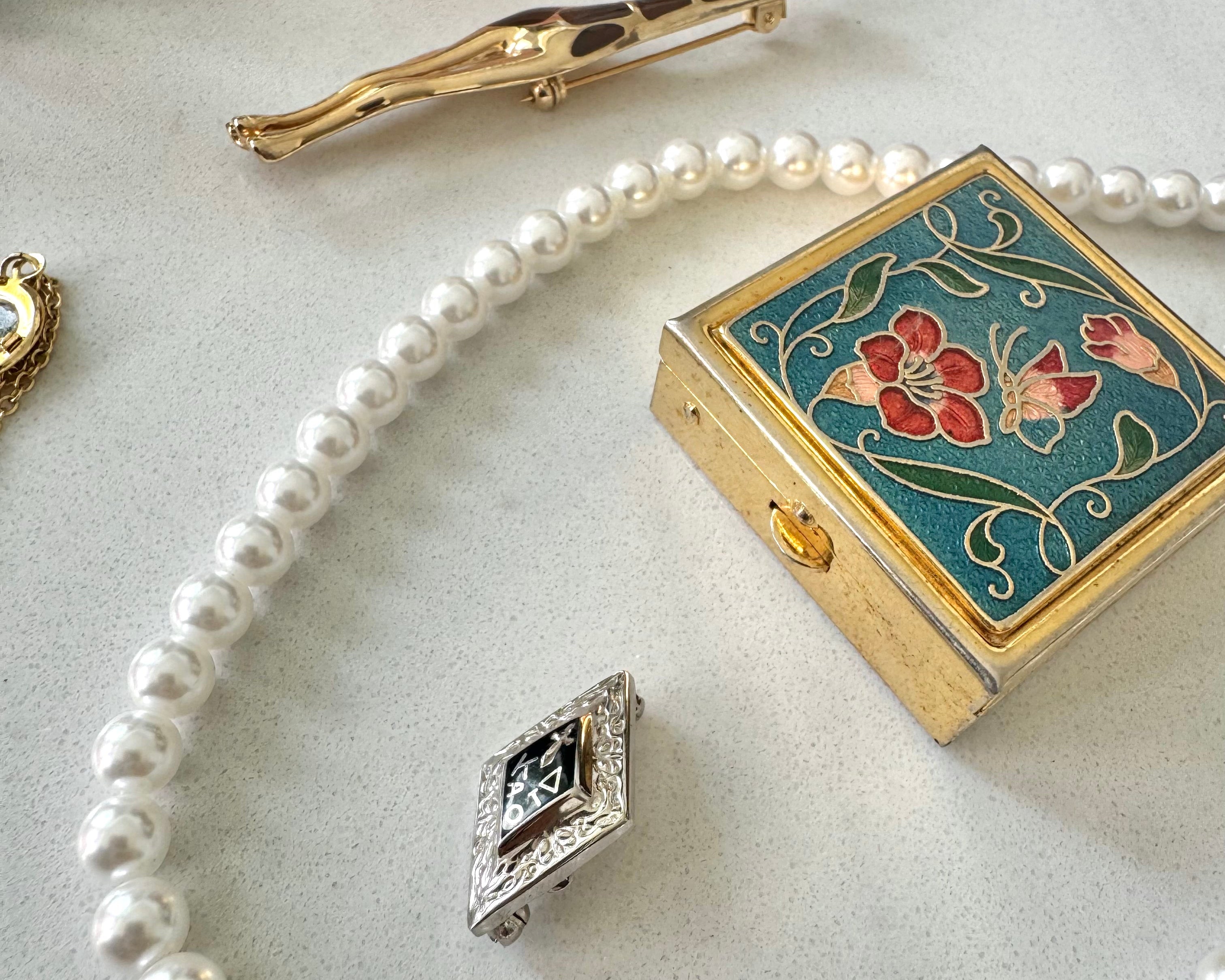 Pearl necklace, decorative box, and brooch on a textured surface
