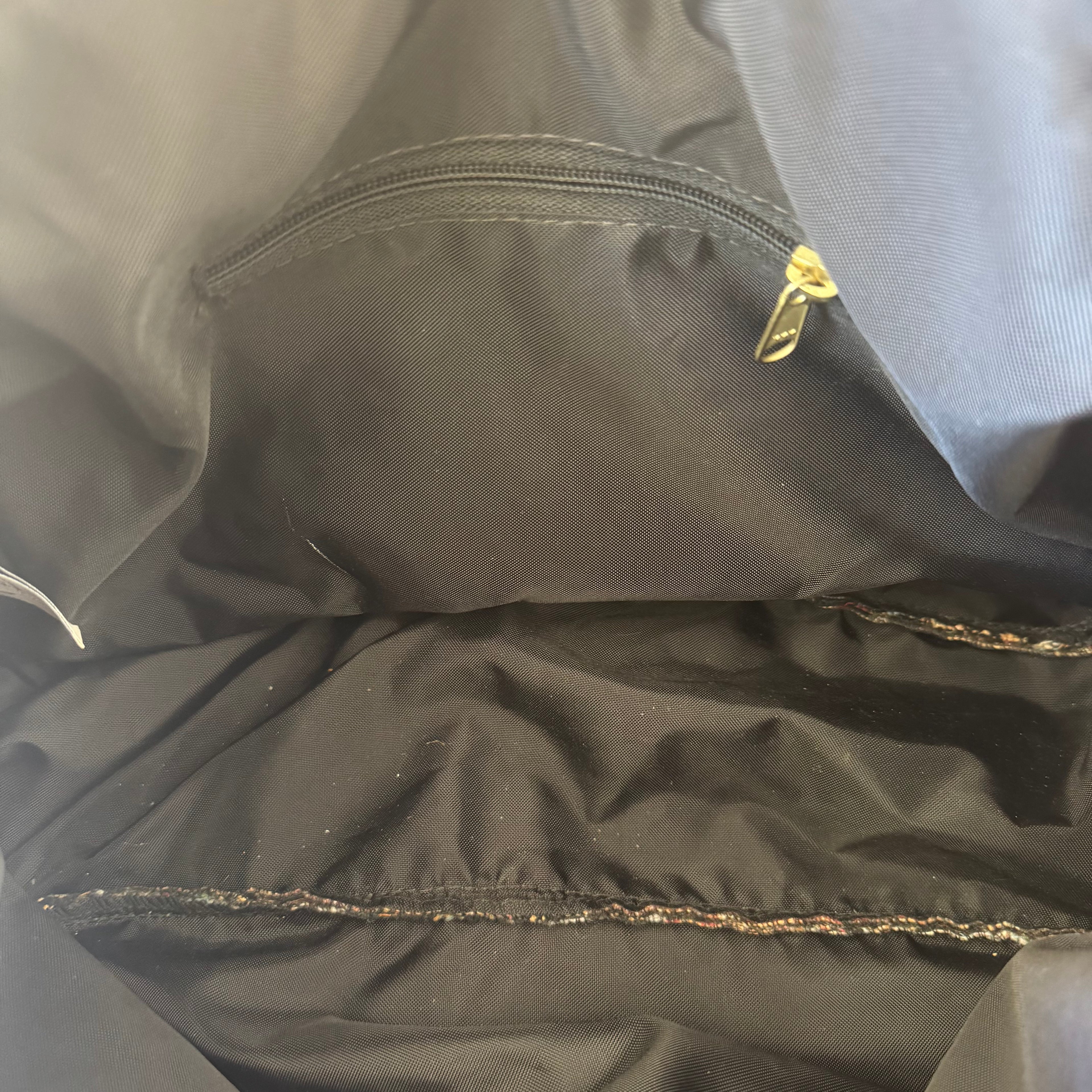 Close-up of the interior of a black jacket or bag, showing a zippered pocket with a gold zipper pull and stitched seam details.