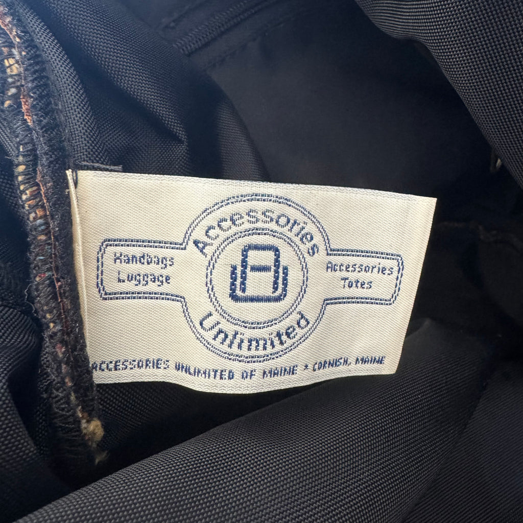 A close-up of a sewn-on fabric label reading 'Accessories Unlimited' with 'Handbags Luggage' and 'Accessories Totes' on a dark navy or black garment interior.