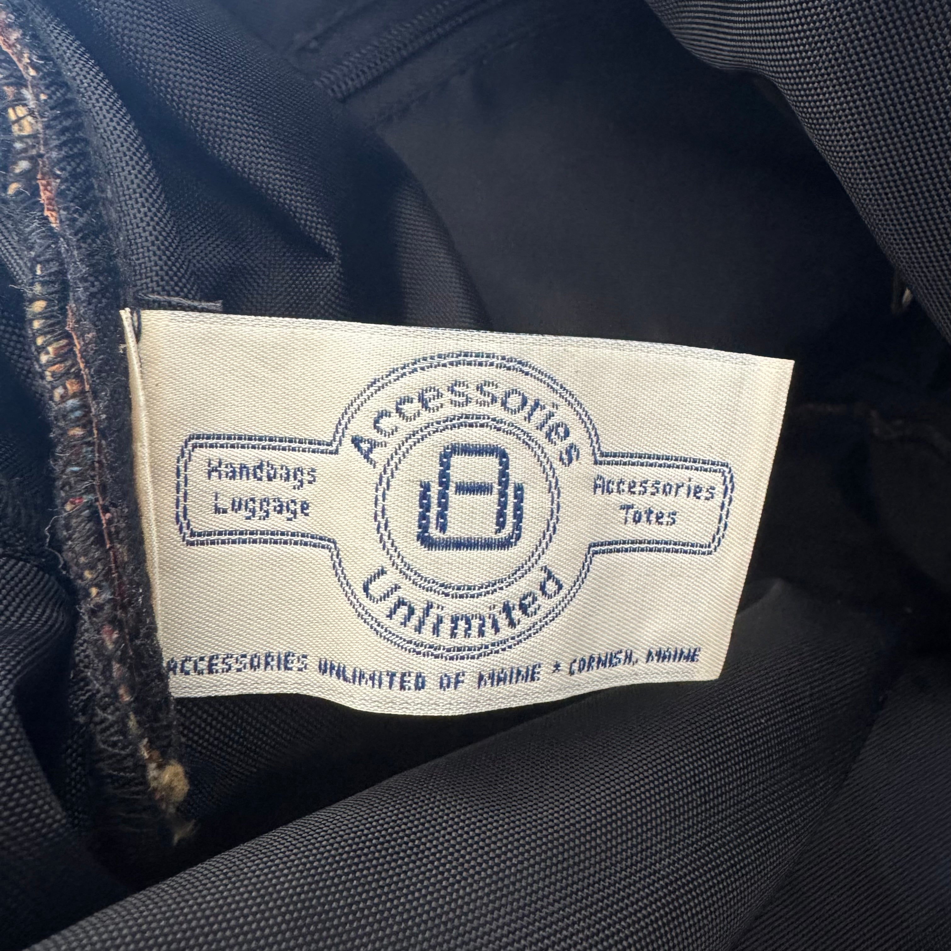 A close-up of a sewn-on fabric label reading 'Accessories Unlimited' with 'Handbags Luggage' and 'Accessories Totes' on a dark navy or black garment interior.