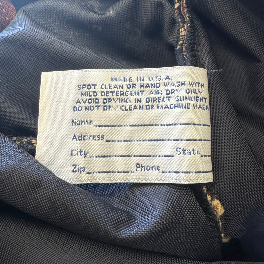 Close-up of a sewn-in care label on dark gray or black fabric, with printed instructions for spot cleaning or hand washing.