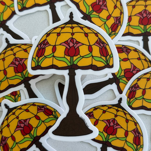Die-cut vinyl sticker featuring an original illustration of a Tiffany-style lamp with a warm amber stained glass shade decorated with red and pink tulips on a dark bronze base
