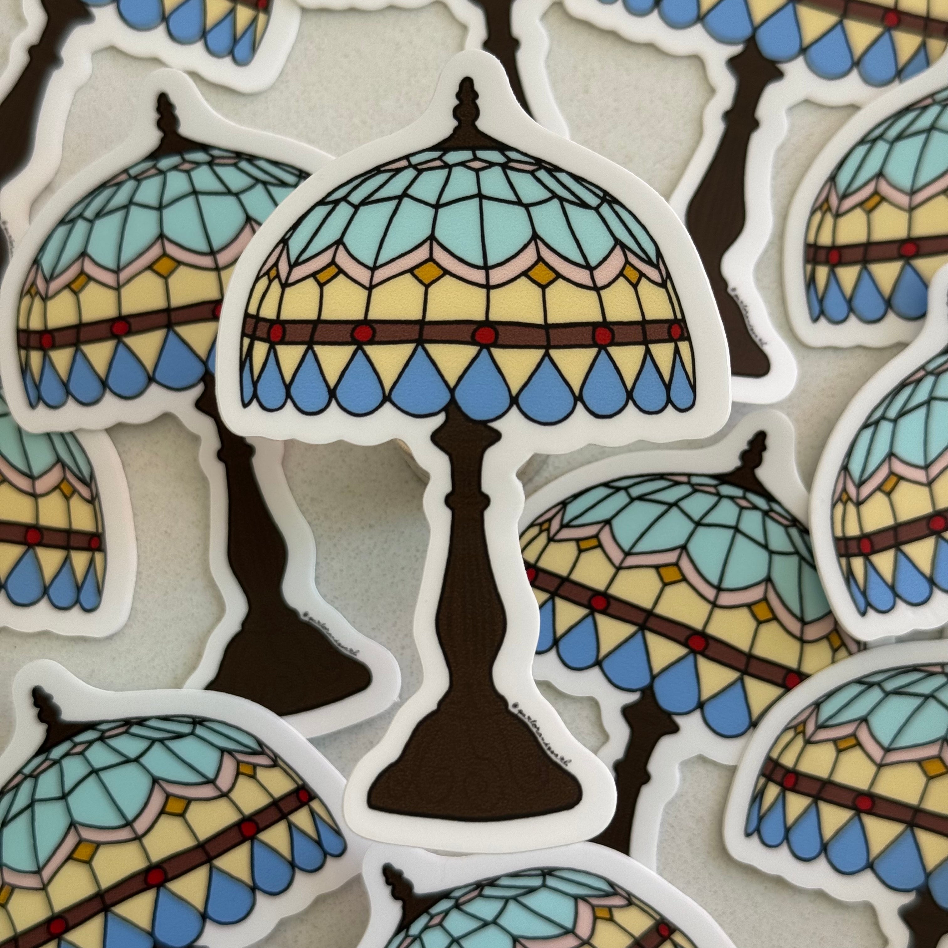 Die-cut vinyl sticker featuring an original illustration of a Tiffany-style lamp with a blue and cream geometric teardrop stained glass shade and dark bronze base