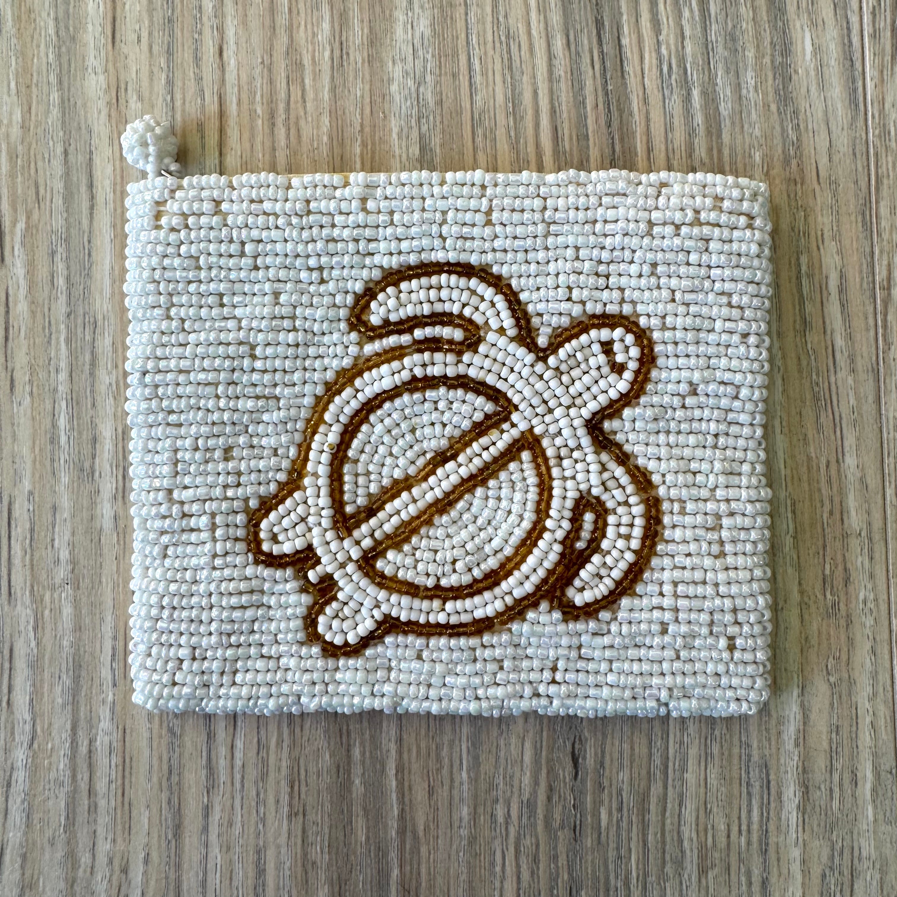 Vintage white iridescent seed bead coin purse with gold bead sea turtle motif on a light wood surface