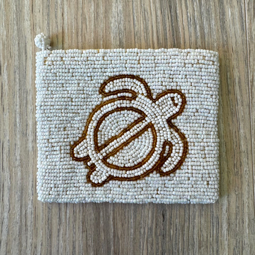 Vintage white iridescent seed bead coin purse with gold bead sea turtle motif on a light wood surface